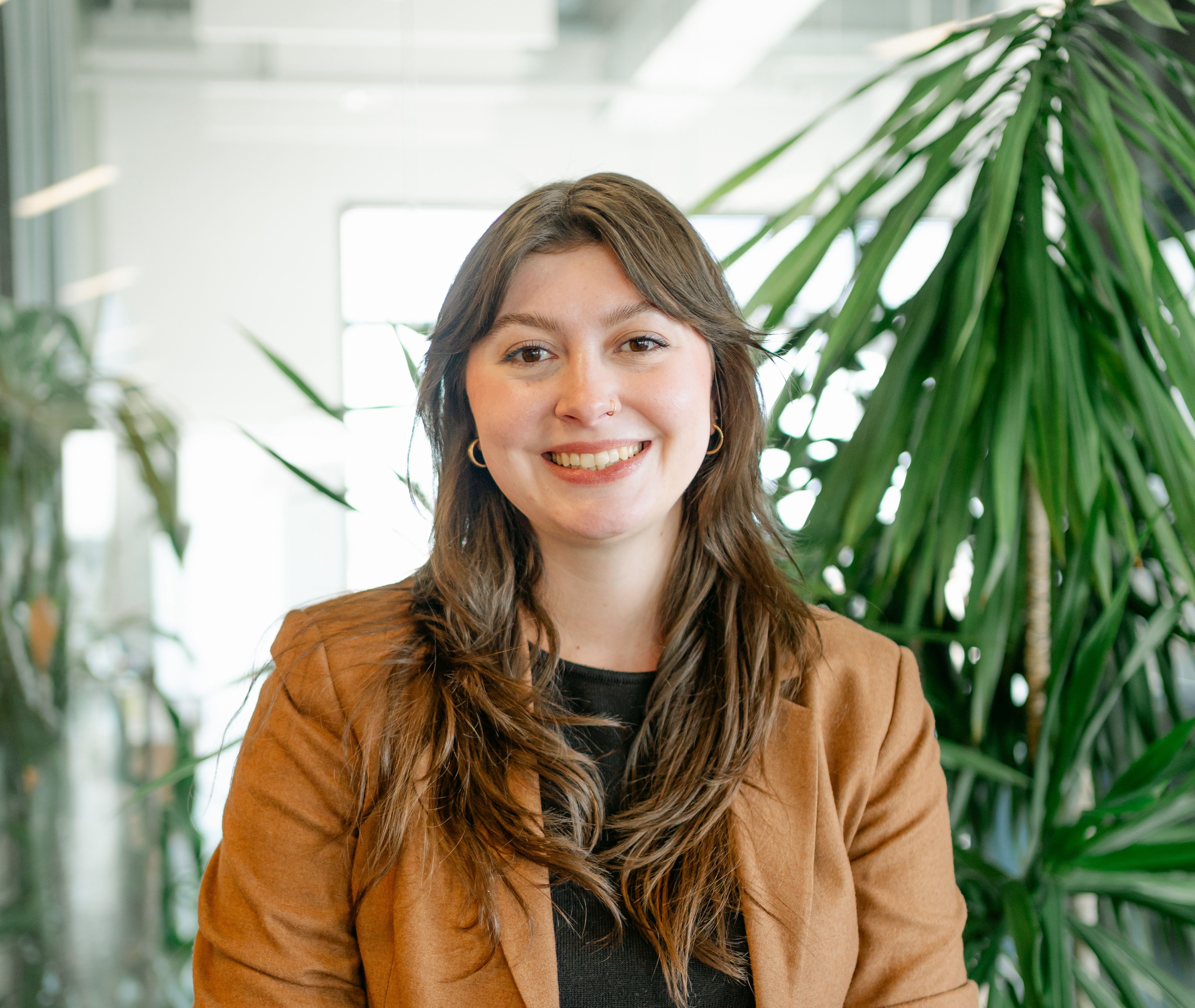 Mackenzie smiles in a brightly lit room with tropical indoor plants