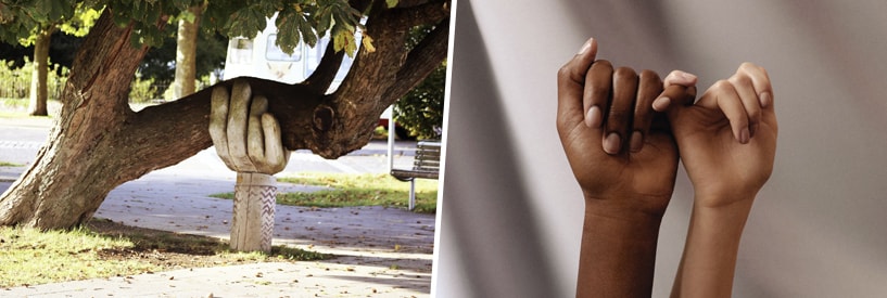 A sculpture shaped like a hand holding up a leaning tree in the park; two hands in a pinky promise