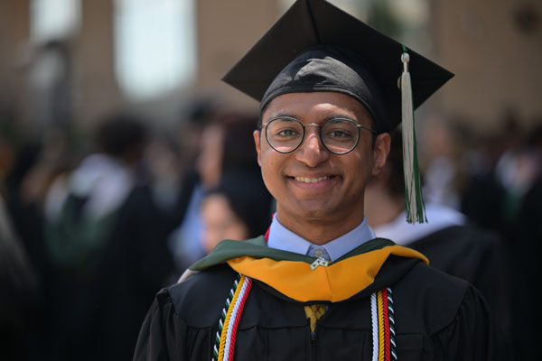 A man in a graduation cap and gown smiles at the camera.