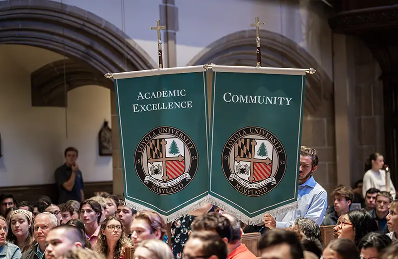 Student holds up two banners that say Academic Excellence and Community during a full mass on campus