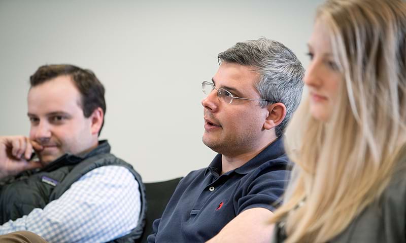 A male student speaking in class while sitting between two other students