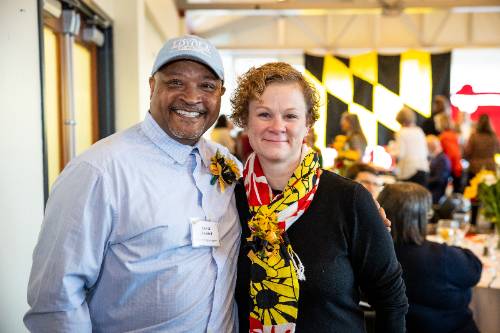 Man with blue shirt and women with sunflower scarf and black sweater smiling.