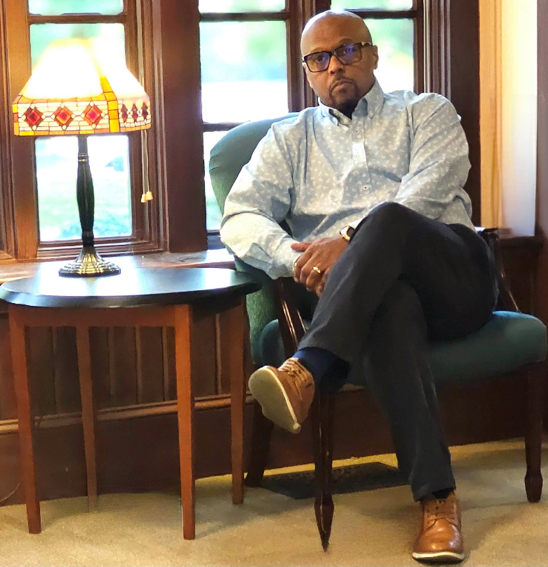 Man sitting on a chair with his legs crossed. Looking straight at the camera.