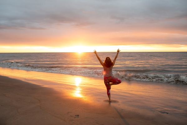 Sunrise on the beach with a woman doing yoga on the shore