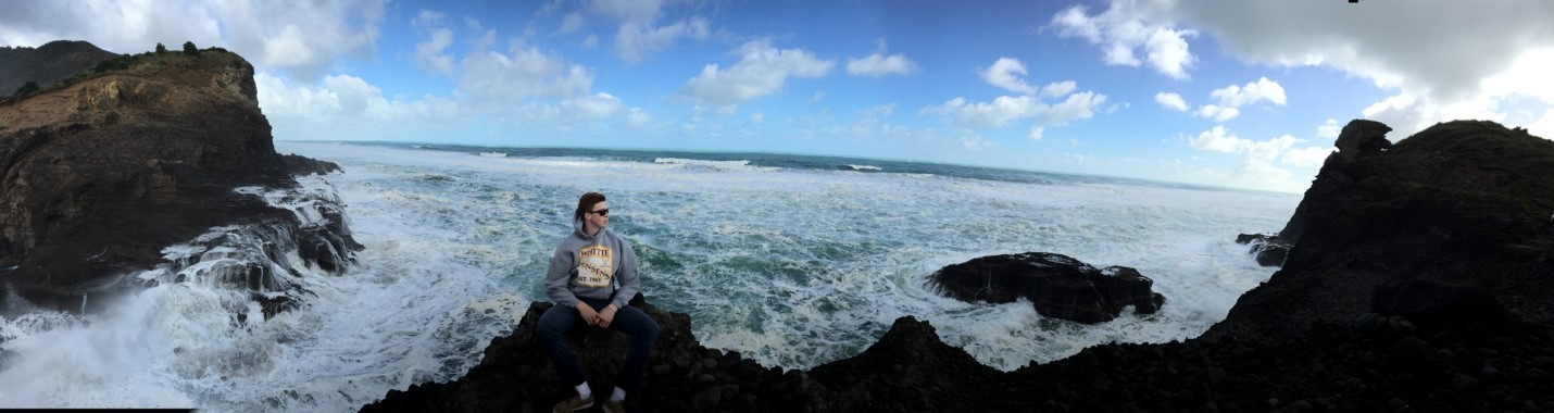 A woman sitting on a rock with the Pacific Ocean behind her as waves crash onto the rocks.