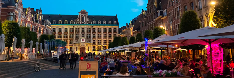 A lively and beautifully lit city street at dusk in Leuven Belgium where there are people enjoying company and eating on the patios of resturants