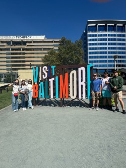People standing next to a sign that says "Visit Baltimore".