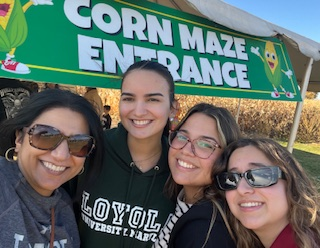 People standing infront of a sign that says "corn maze enterance".