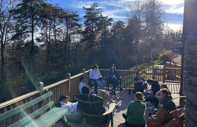 Students sitting on a deck outside, with trees in the background