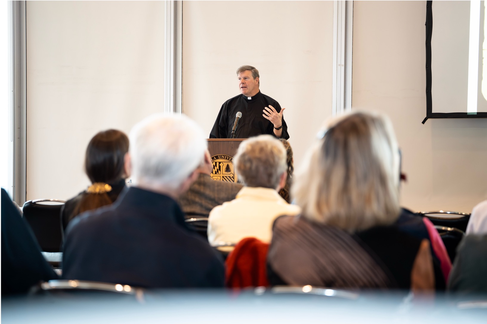 A priest in front of a podium talking to a group of people