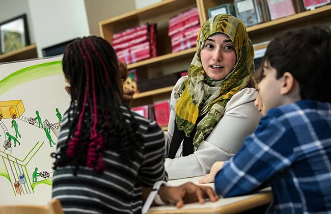 A teacher instructing two young children in a classoom