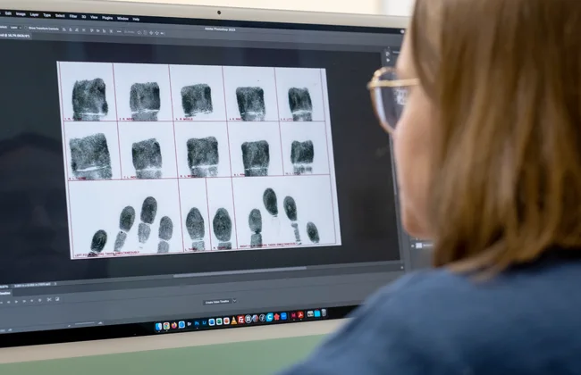A female with glasses looking at a computer screen showing fingerprints