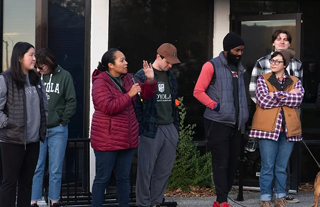 A crown, including Loyola students, gathers outside of a building. One person is talking with a microphone