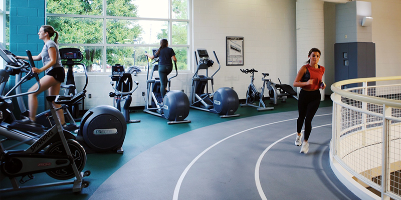 Student running the curve of the indoor track while passing students on elyptical machines placed on the perimeter