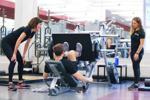 Student using a leg press machine while two trainers observe