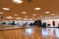 Fitness studio with wood floors, large mirrors, and plenty of exercise equipment against one wall