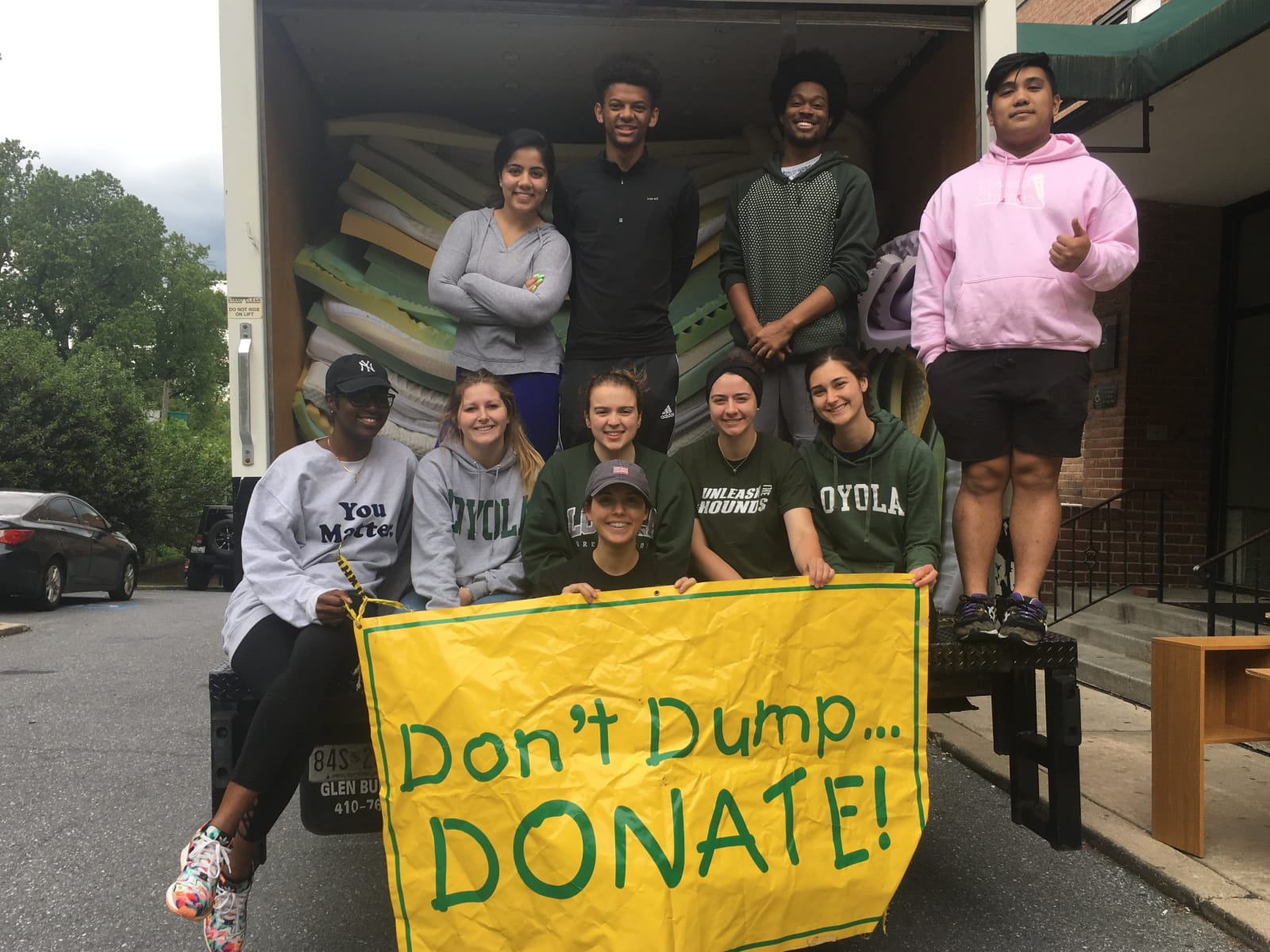 a group of students standing in the back of a moving truck holding banner reading Don't Dump, Donate!
