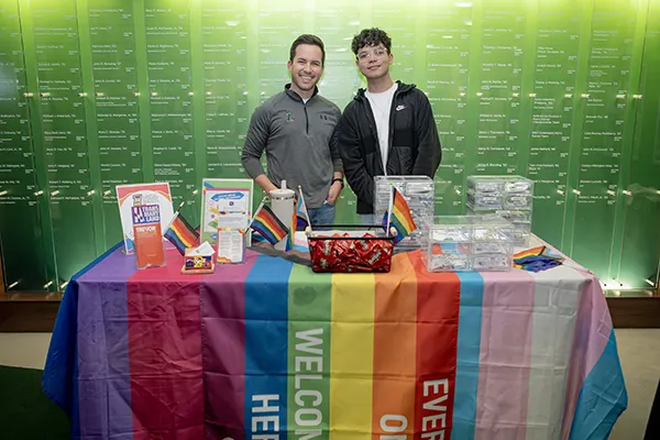 A staff member and student stand at an LGBTQ+ table event