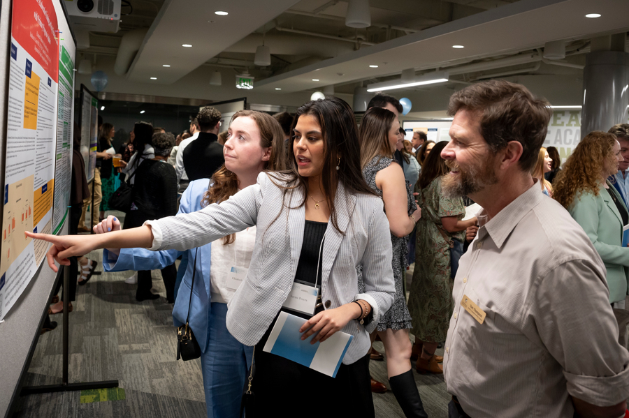 Two graduate students present their poster to a faculty member at Emerging Scholars 2024