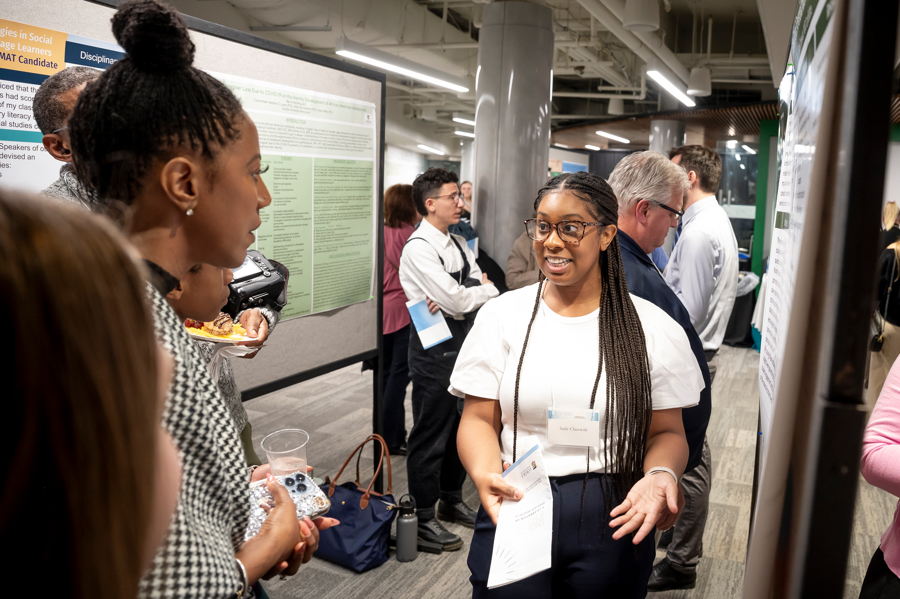 Presenter gestures in front of poster at Emerging Scholars poster session 2024