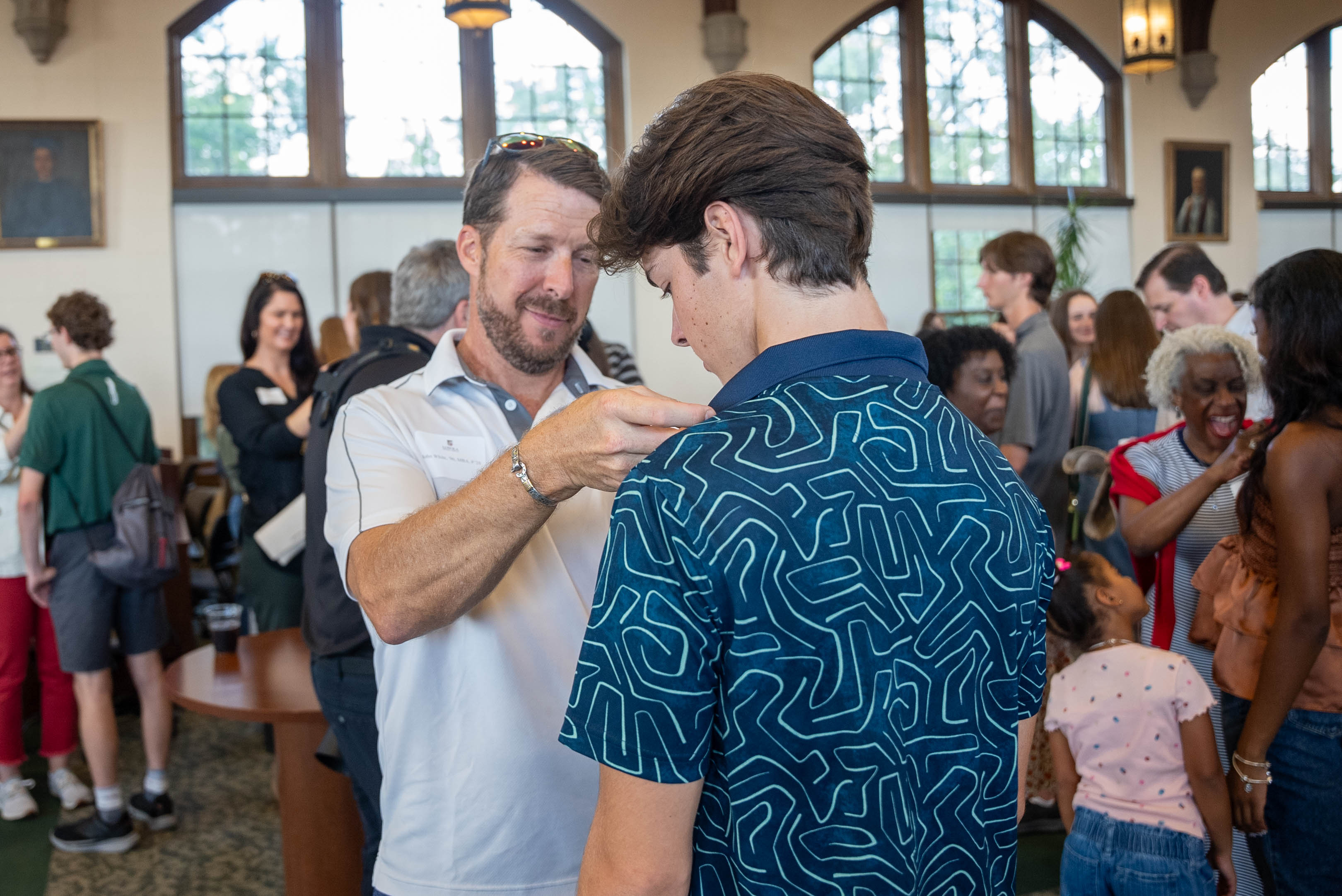 A father puts an alumni pin on his son