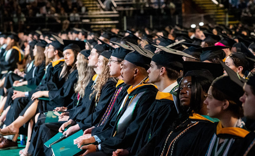 Students sitting and wearing black and hold commencement gowns 