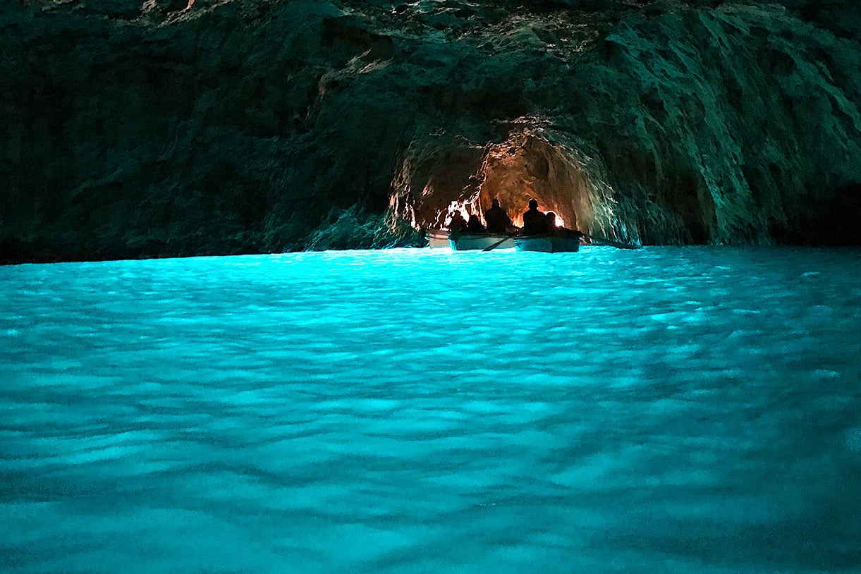 Silhouettes in boats floating in a cave with the water glowing a bright blue