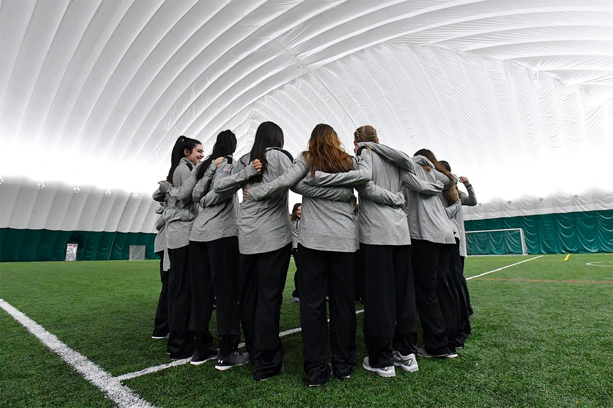 Loyola athletes huddling with a silver-white dome surrounding them and a practice field