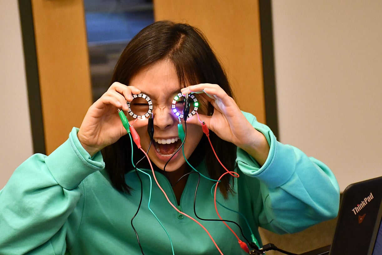 A student putting round electronic devices over her eyes like glasses and smiling