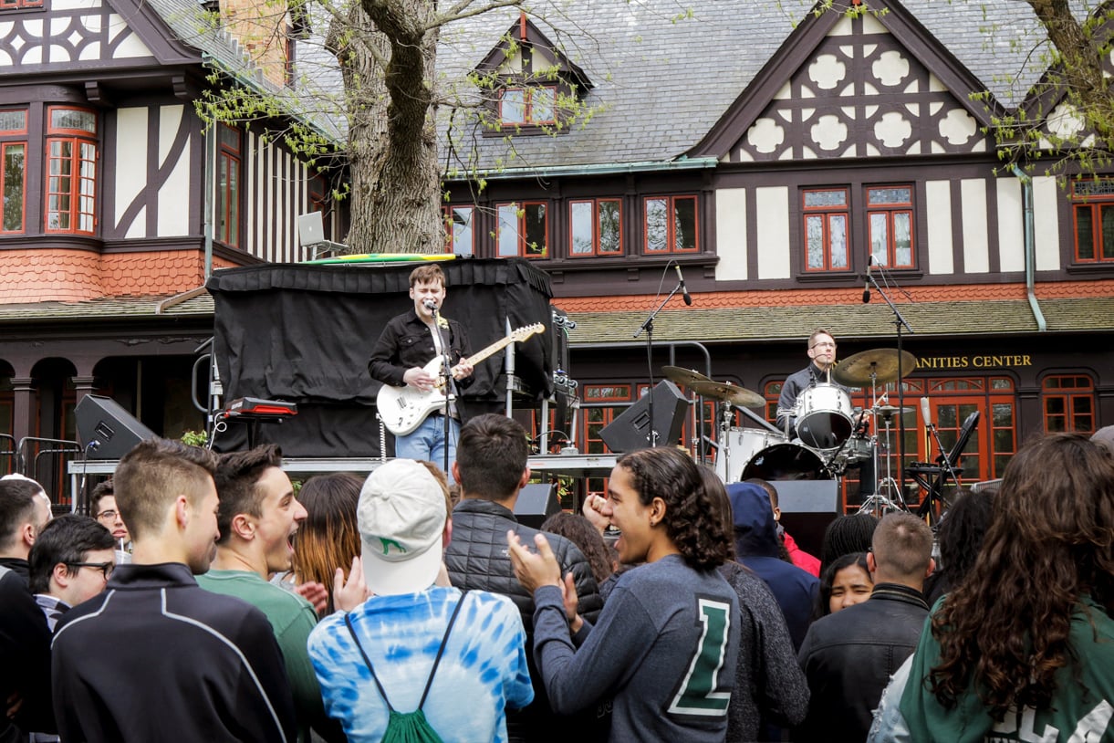 A band performs in front of the Loyola Humanities building, with a crowd cheering in the foreground