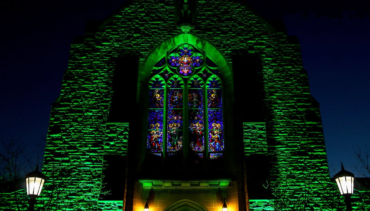 The front of the Alumni Memorial Chapel lit up by green lighting at night