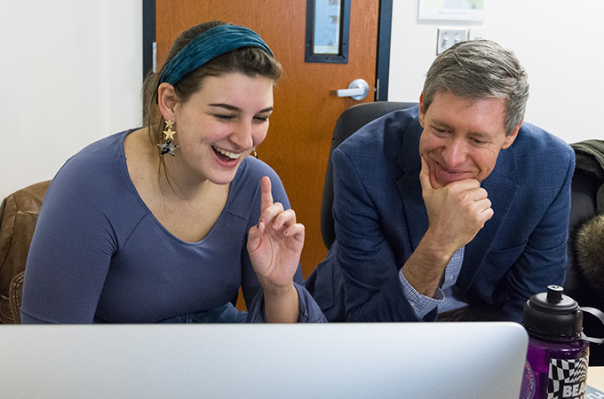 Professor Atticks and student laugh while looking at the computer.