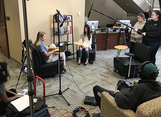 Group of students with video, lighting, and audio equipment filming two other students sitting down