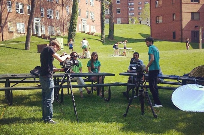 Group of students setting up cameras outside; other students sitting at benches to be filmed