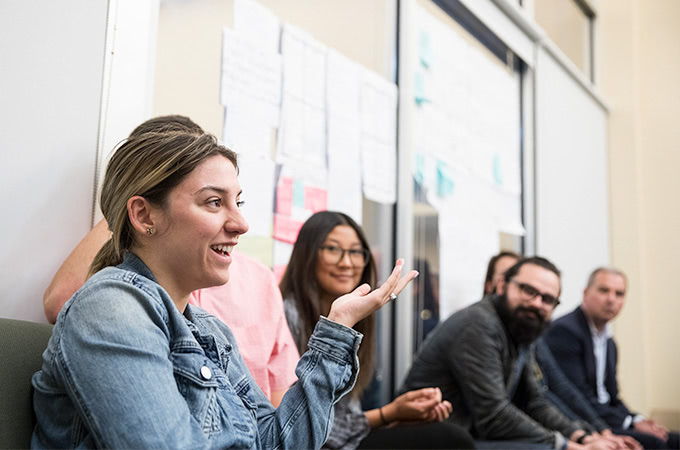 Students sitting along a wall chatting in front of ideas taped to the wall