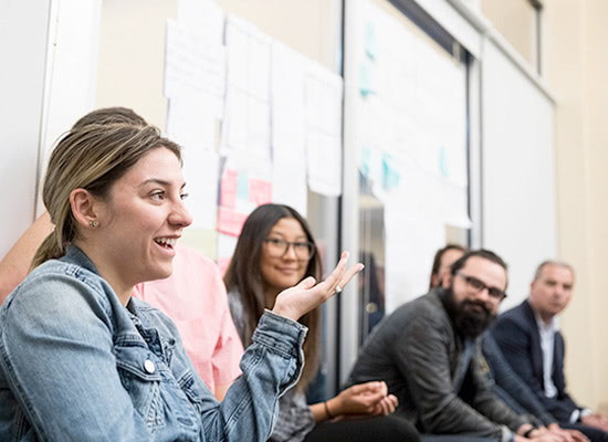 Students sitting along a wall chatting in front of ideas taped to the wall