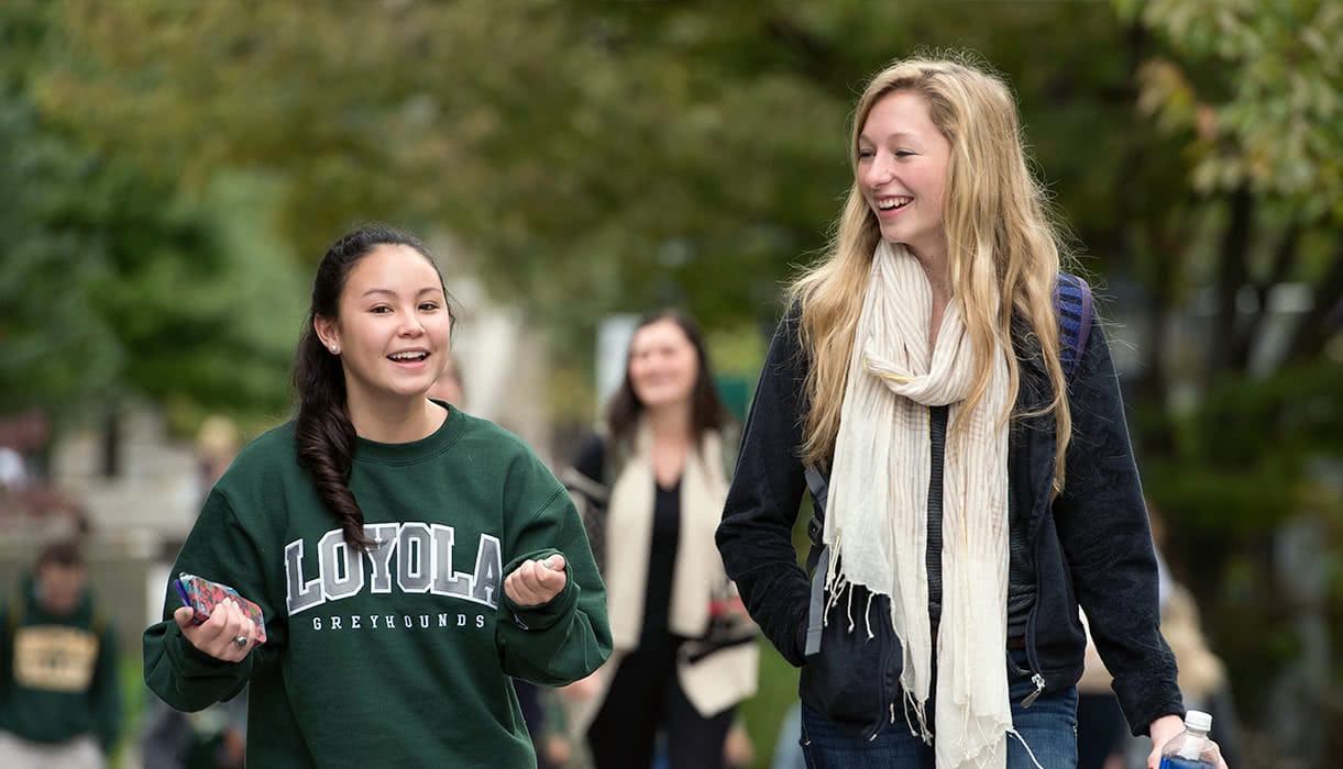 Two students smile and talk while walking through Loyola's campus