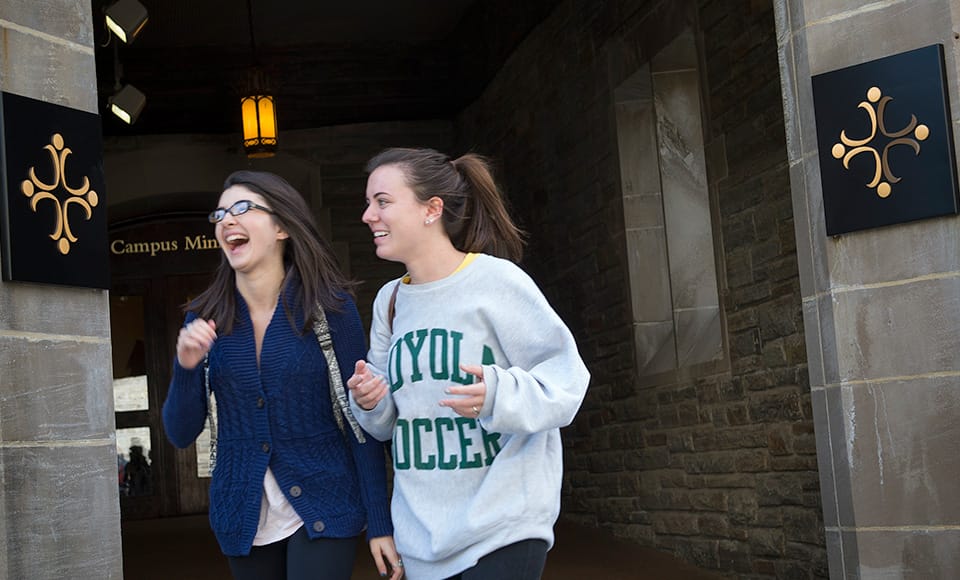 Two female students walking in front of a campus ministry sign