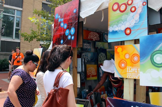 People at an art stand where paintings are hanging for sale