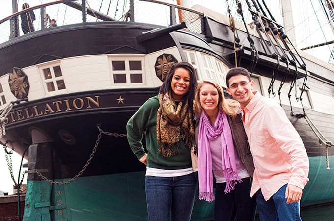 Three students posing in front of the U.S.S. Constellation ship