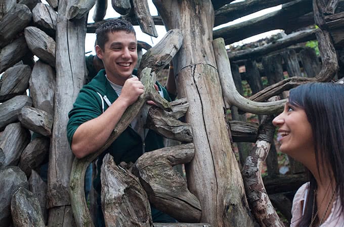 Two students climbing in an art structure made of old wood