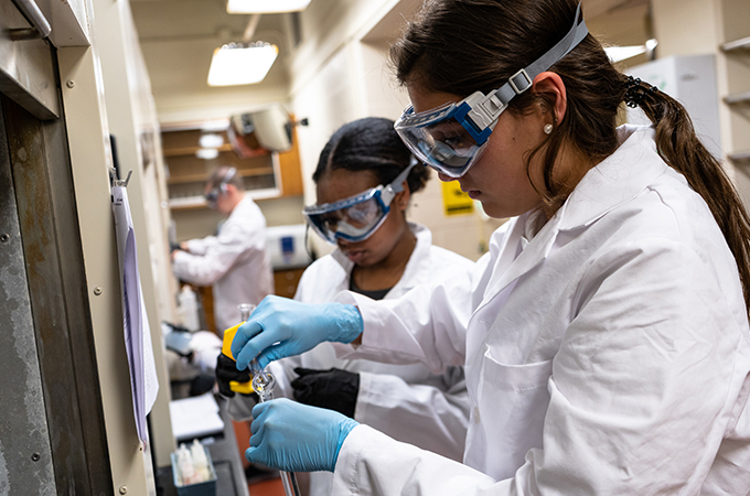 A pair of students pour the solution into a beaker.