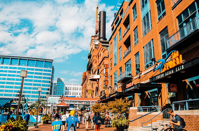 People walk along the harbor next to restraurants in a red-bricked building