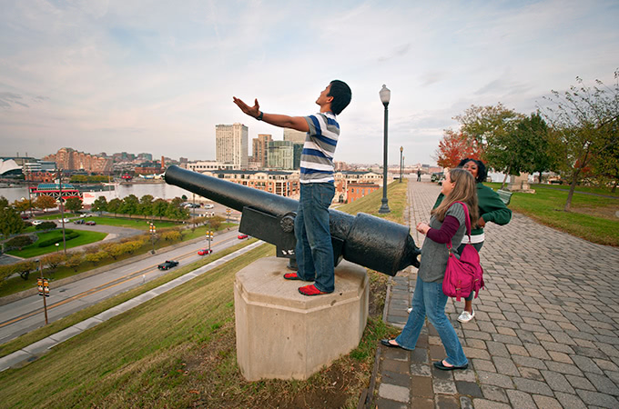 A student stands with his arms out next to a canon in Fed Hill. Other students stand nearby