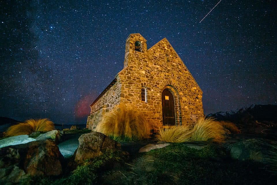 An old, small, stone building sits under the starry, night sky