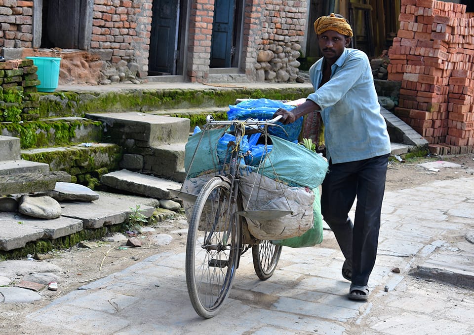 A man walking his bike, which carries multiple bags