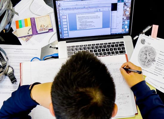 An overhead view of a student studying with a notebook, laptop, and other notes