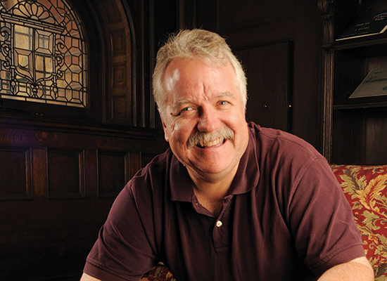 DeVries seated in chair with a stained glass window in the background.