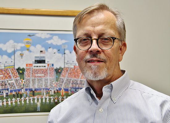 Professor Steve Walters, Ph.D. in front of a painting of a baseball field.