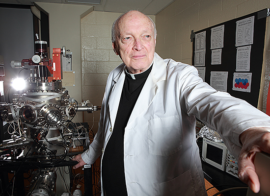 Fr. Haig next to astronomical device in physics lab.